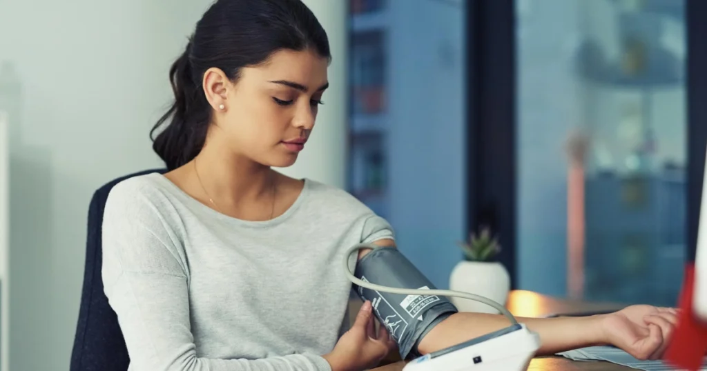 Young woman at a desk taking her blood pressure with a digital arm cuff, focusing on the monitor screen for Chronic disease management in Cedar Park, TX.